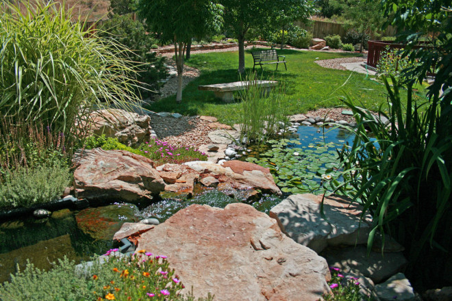 A beautiful water feature with a pond and relaxing bench setting. Cinnamon Shadow Quarry boulders and Siloam slabs create a cascading effect with Wall Stone borders and a custom bench.